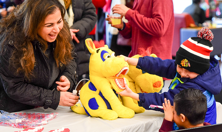 Woman and two boys playing with a yellow and blue stuffed animal.