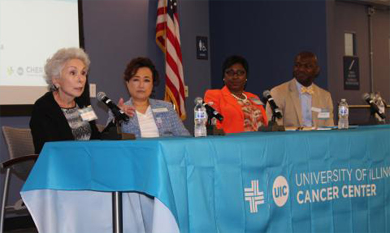 Three women and a man speaking on microphone and sitting down by a blue table.