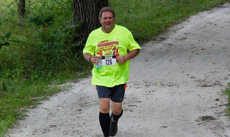 man running by the woods with a running number on his yellow shirt.