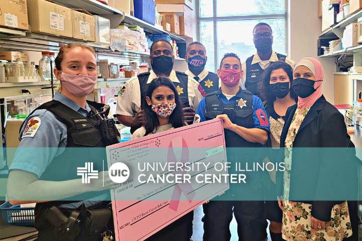 Cancer Center staff members with UIC Police officers in a research lab with a big pink donation check
