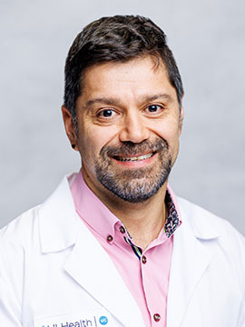 Headshot of Dr. Matias Sanchez wearing a pink shirt and white coat.